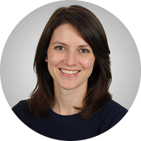 A woman with straight, shoulder-length brown hair and a friendly smile, wearing a dark top, poses against a light gray circular background.